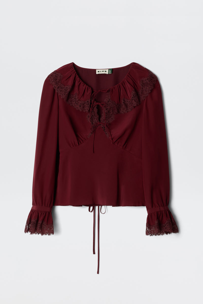 The Aimme - Maroon blouse features long sleeves, lace-trimmed ruffled neckline and cuffs, a tie at the neck, and a drawstring cinched waist, shown against a plain light background.