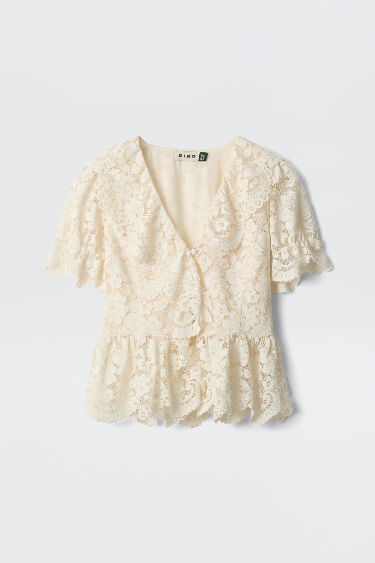 Dollie - Cream: A cream-colored lace blouse featuring short sleeves, a V-neckline, ruffled hem, and scalloped edges, shown against a plain white background.
