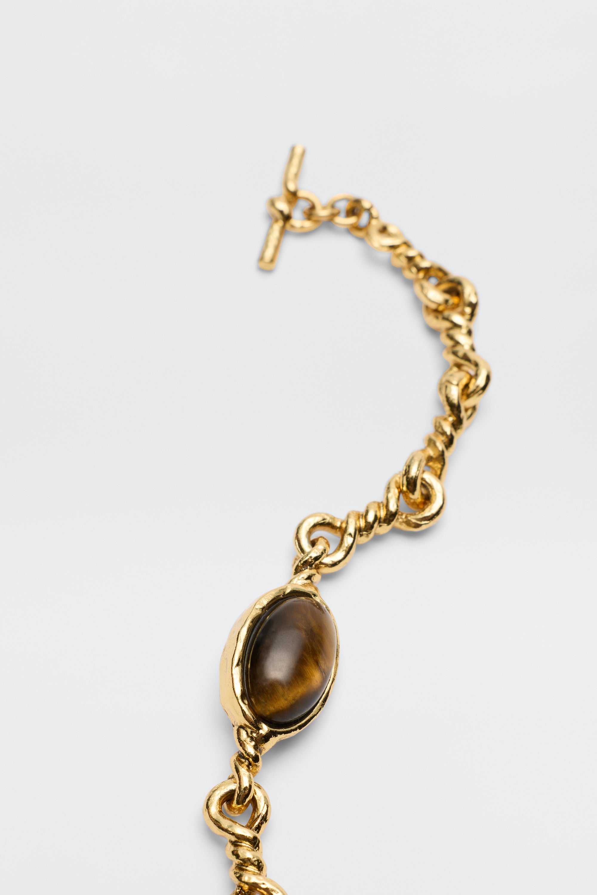The Maelis - Gold is a chunky gold-plated bracelet with a twisted design and an oval tiger's eye gemstone in a gold bezel, shown on a light gray background—ideal for fans of vintage-inspired jewelry.