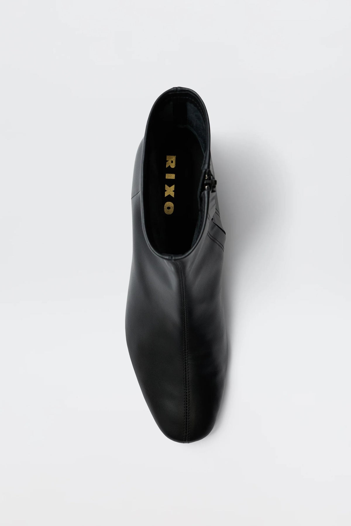 Top view of the Rey - Black Leather ankle boot, featuring a rounded toe and visible gold RIXO branding on the insole, set against a plain white background.