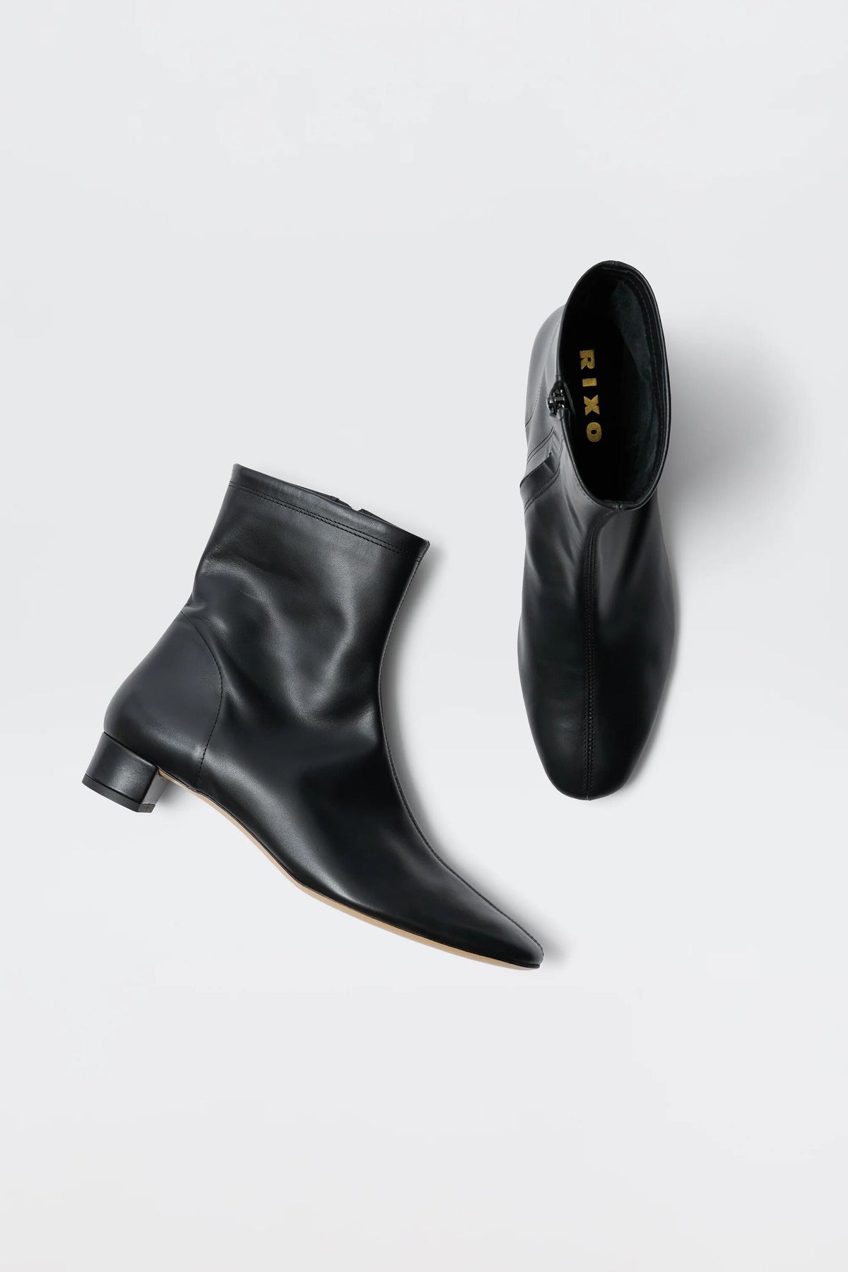 The Rey - Black Leather boots are shown on a white background: two ankle boots with a short square heel, pointed toe, side zipper, and RIXO label inside—perfect vintage-inspired footwear.