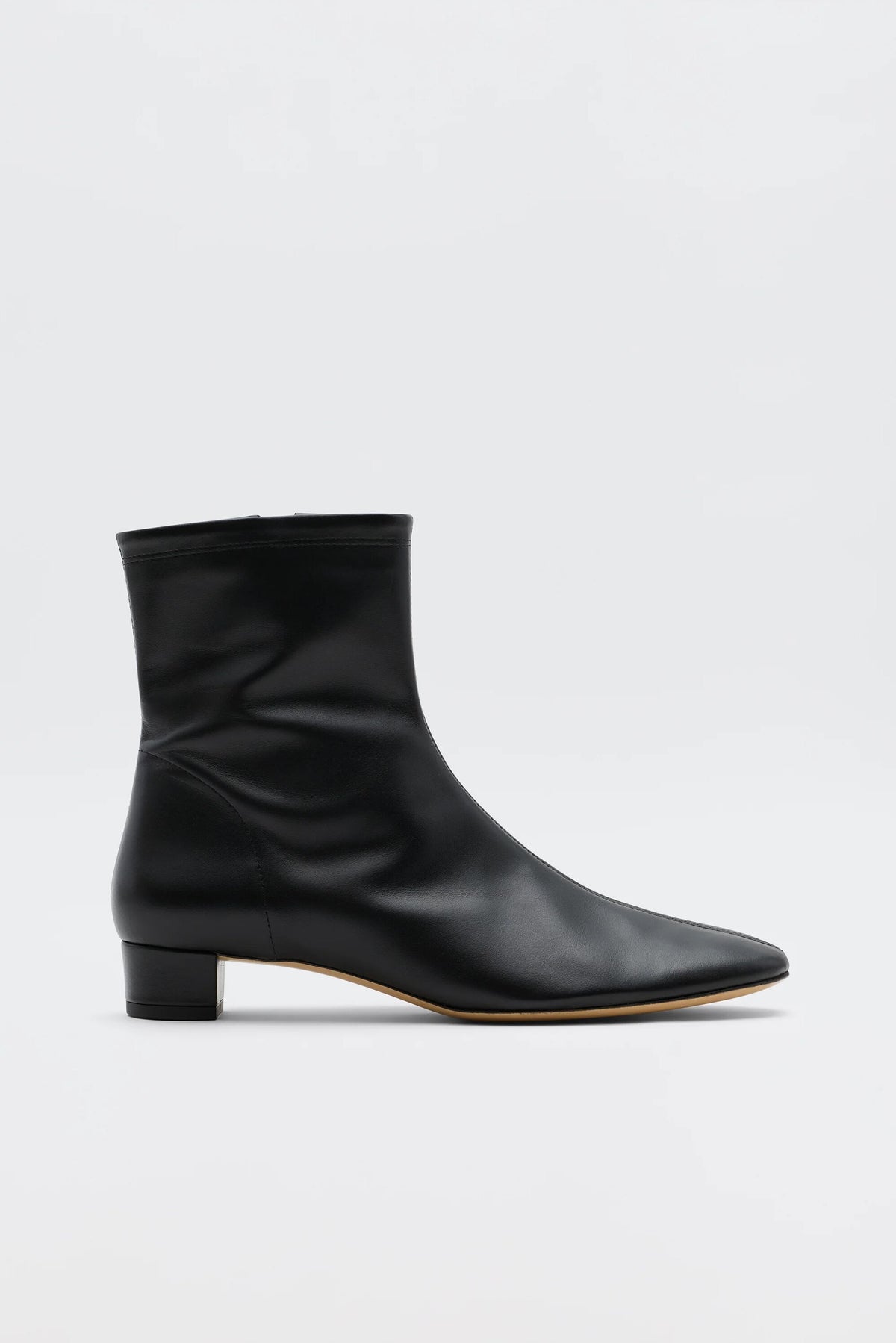 The Rey - Black Leather ankle boot features a low heel, pointed toe, and minimalist design for vintage-inspired elegance. Its sleek side profile stands out in smooth black leather against a plain white background.