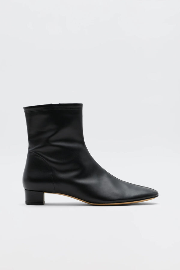 The Rey - Black Leather ankle boot features a low heel, pointed toe, and minimalist design for vintage-inspired elegance. Its sleek side profile stands out in smooth black leather against a plain white background.