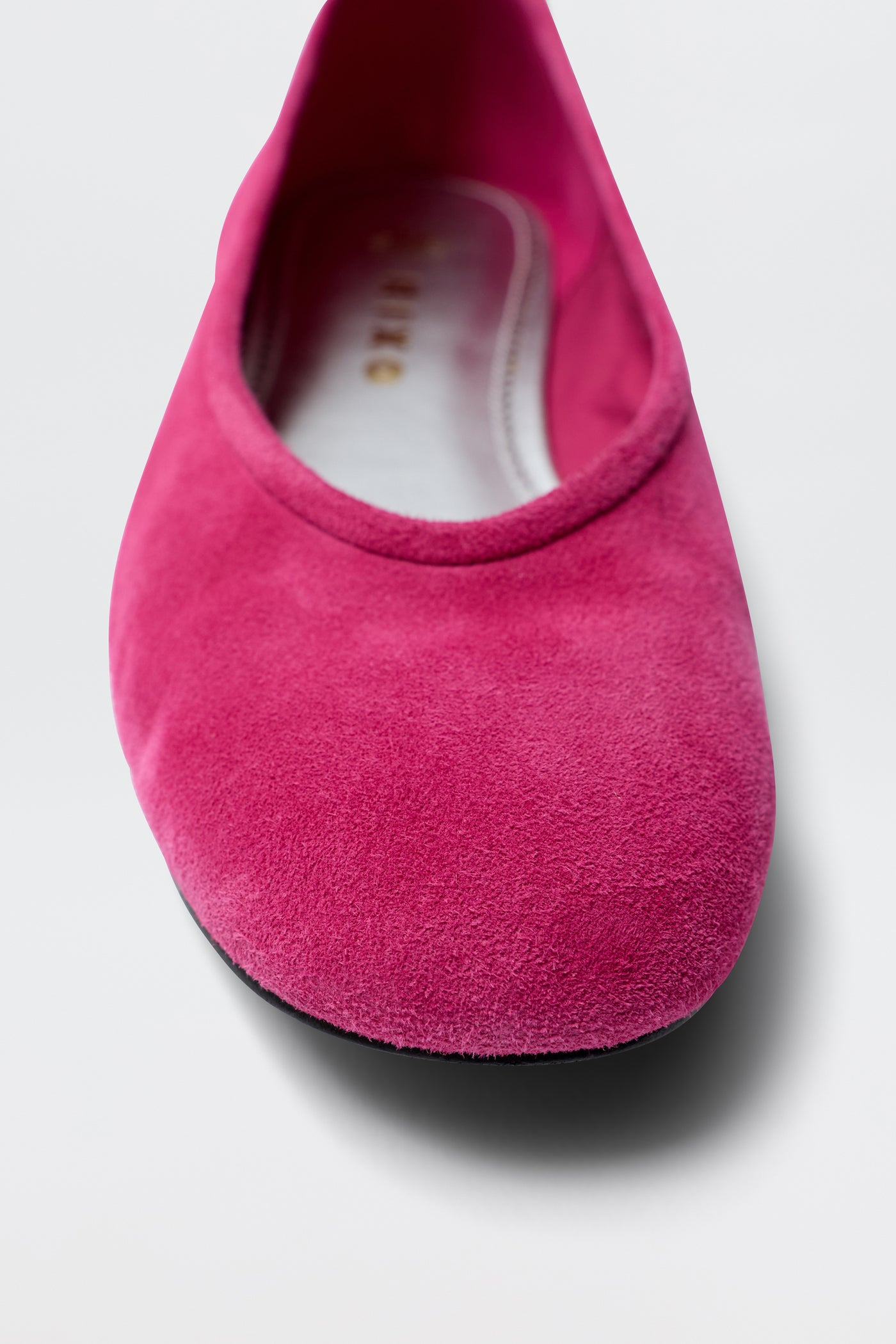 A close-up of the Mirielle - Pink suede ballet flat shows its rounded toe and gold-lettered insole on a light background—ideal for those who love elegant pink suede shoes.