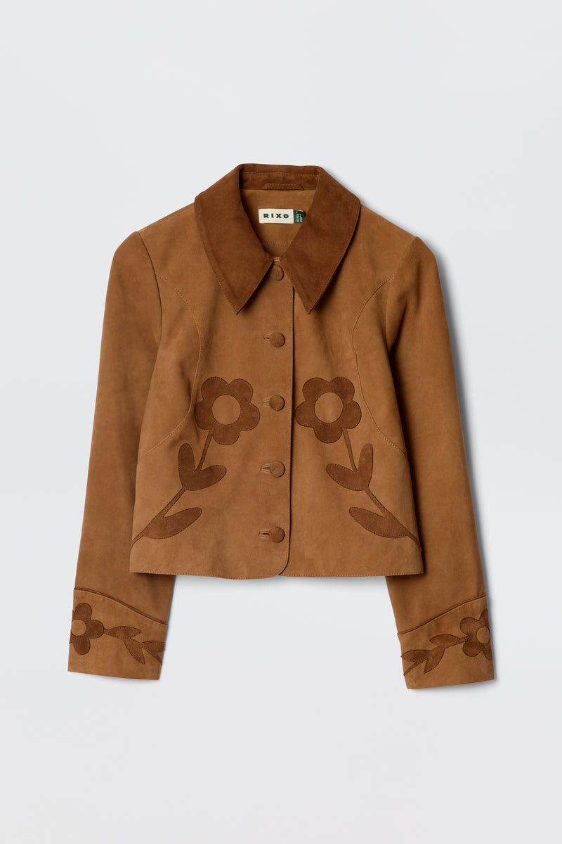 The Dionne - Retro Daisy is a brown suede jacket featuring a wide collar, button-up front, and decorative dark brown floral patterns on the front and cuffs, inspired by classic vintage souvenir jacket styles.