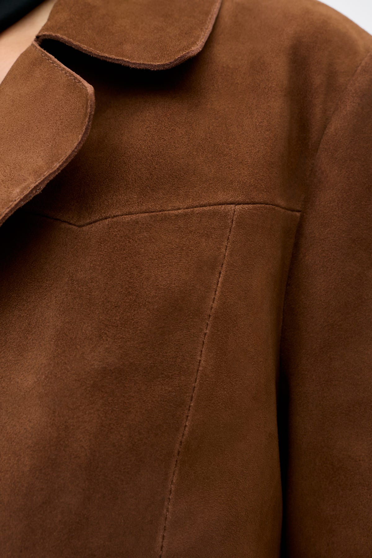 Close-up of the Lainey - Chestnut jacket in brown suede, highlighting the soft texture, a seam, and part of the collar against a neutral background.