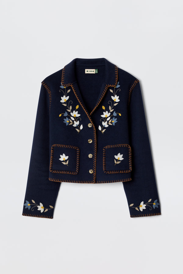 The Sunday - Petal Embroidery Navy is a luxurious cropped jacket in navy wool blend, featuring floral embroidery on the front and lapels, brown decorative edge stitching, and silver buttons.