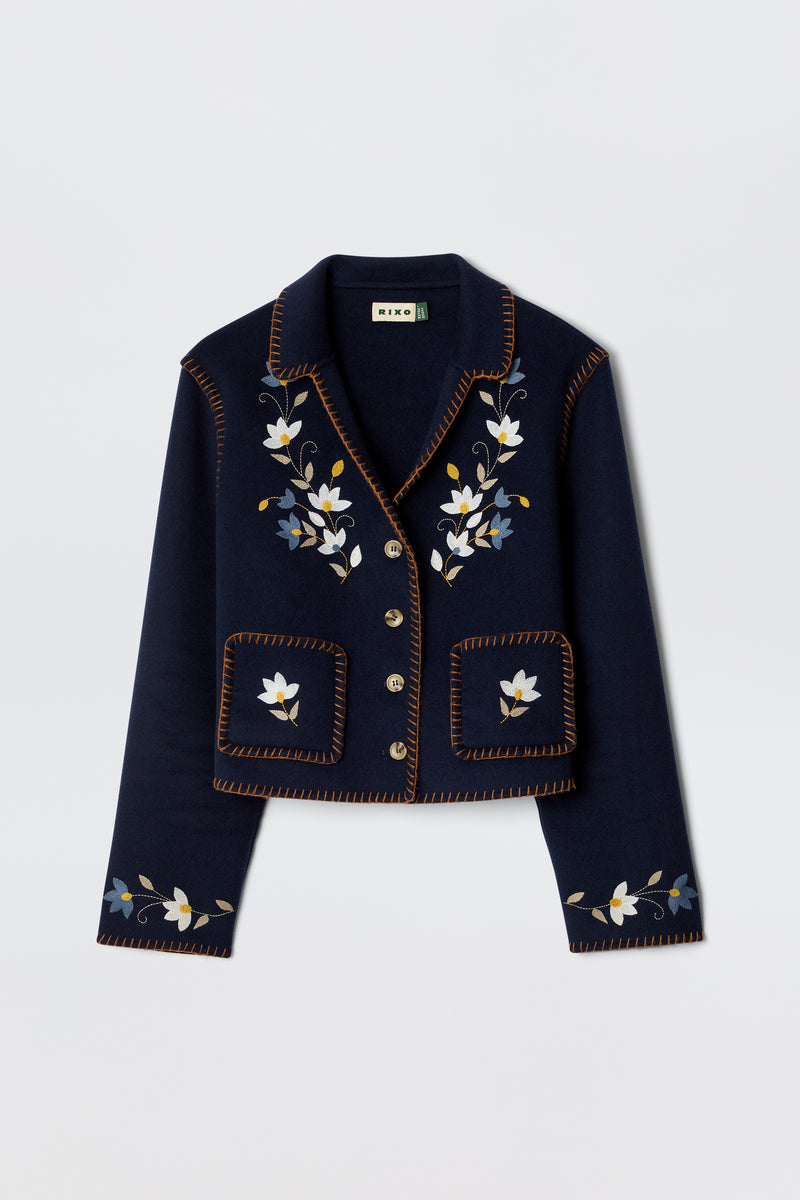 The Sunday - Petal Embroidery Navy is a luxurious cropped jacket in navy wool blend, featuring floral embroidery on the front and lapels, brown decorative edge stitching, and silver buttons.