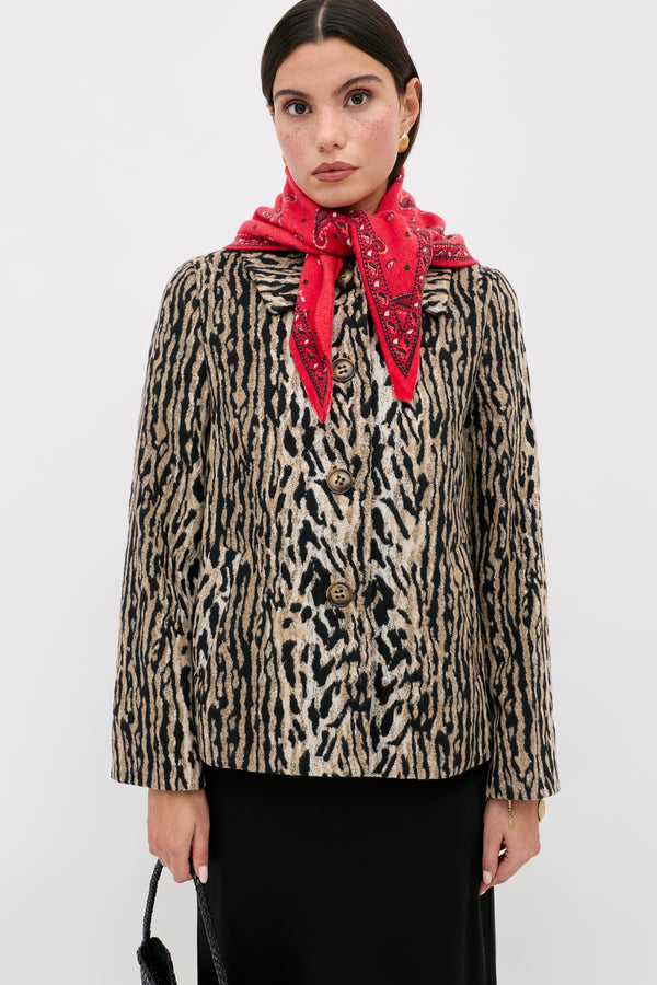 A woman wearing the Tommie - Bohemia Leopard jacket and a red bandana scarf stands against a white background, holding a black handbag and looking at the camera.