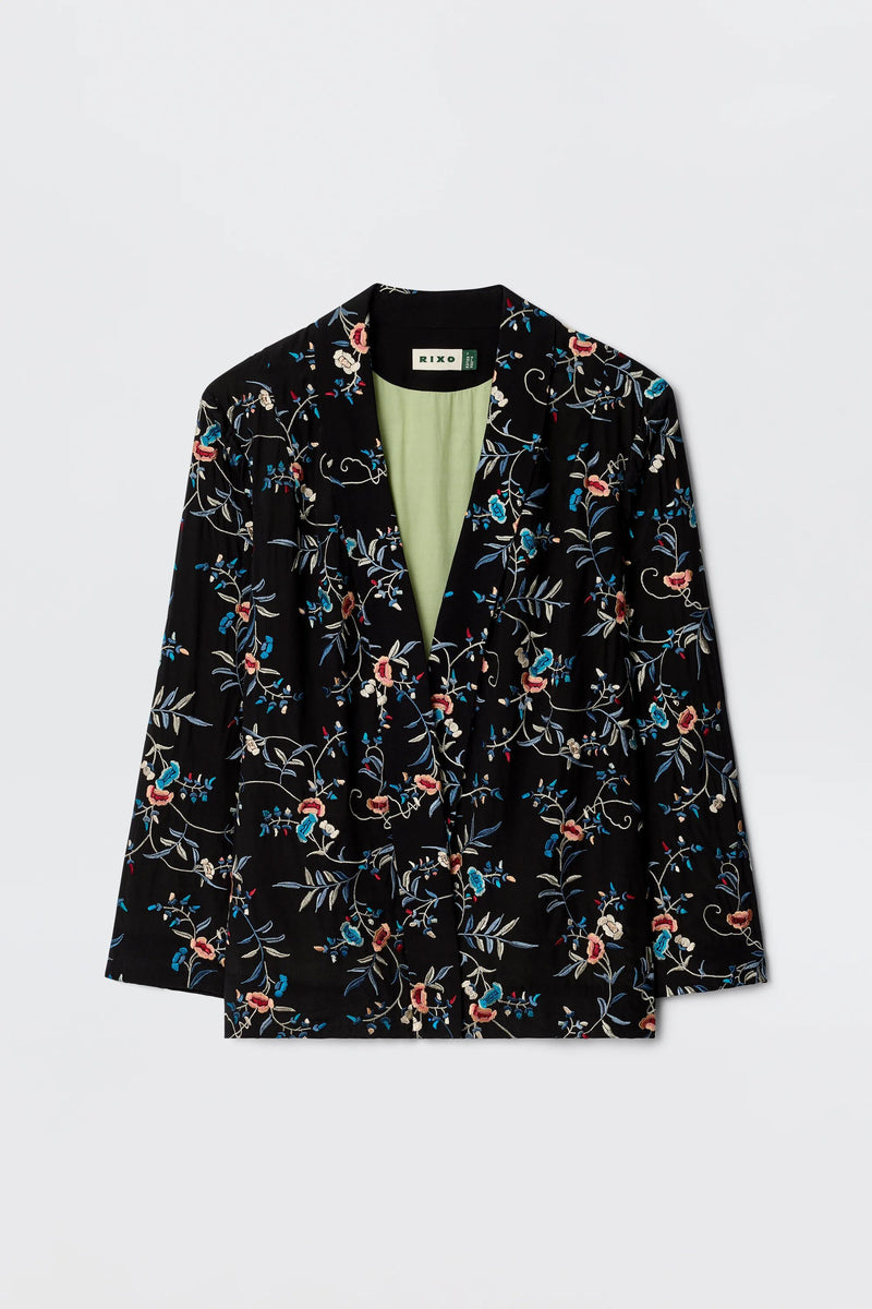 The Malachy - Botanical Embroidery Black is a black blazer with red, blue, and white embroidered botanical motifs, a light green lining, made from lightweight crepe. Shown on a plain white background.