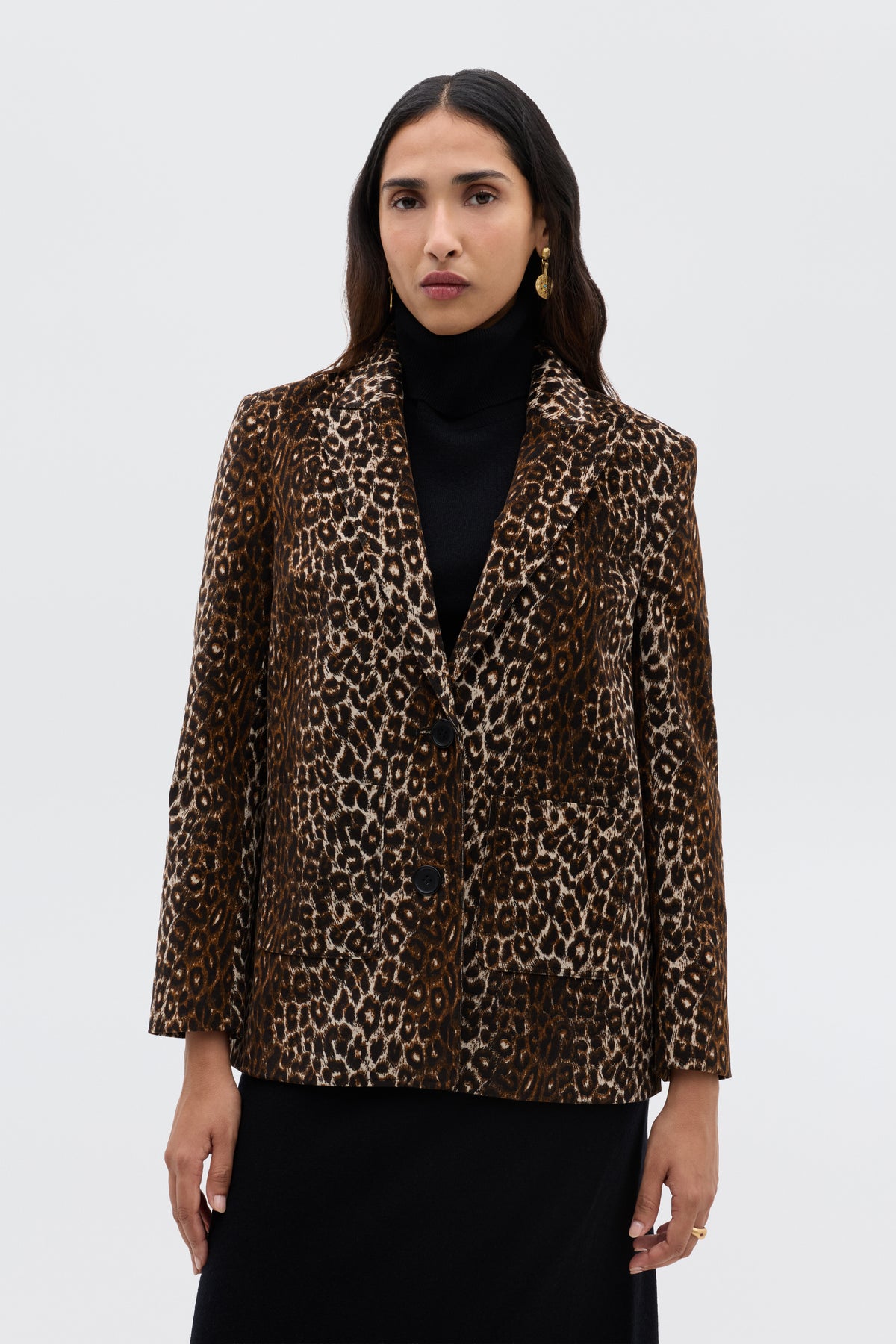 A woman with long dark hair wears the Xander - Lyra Leopard Black jacket over a black turtleneck and skirt, standing against a plain light background.