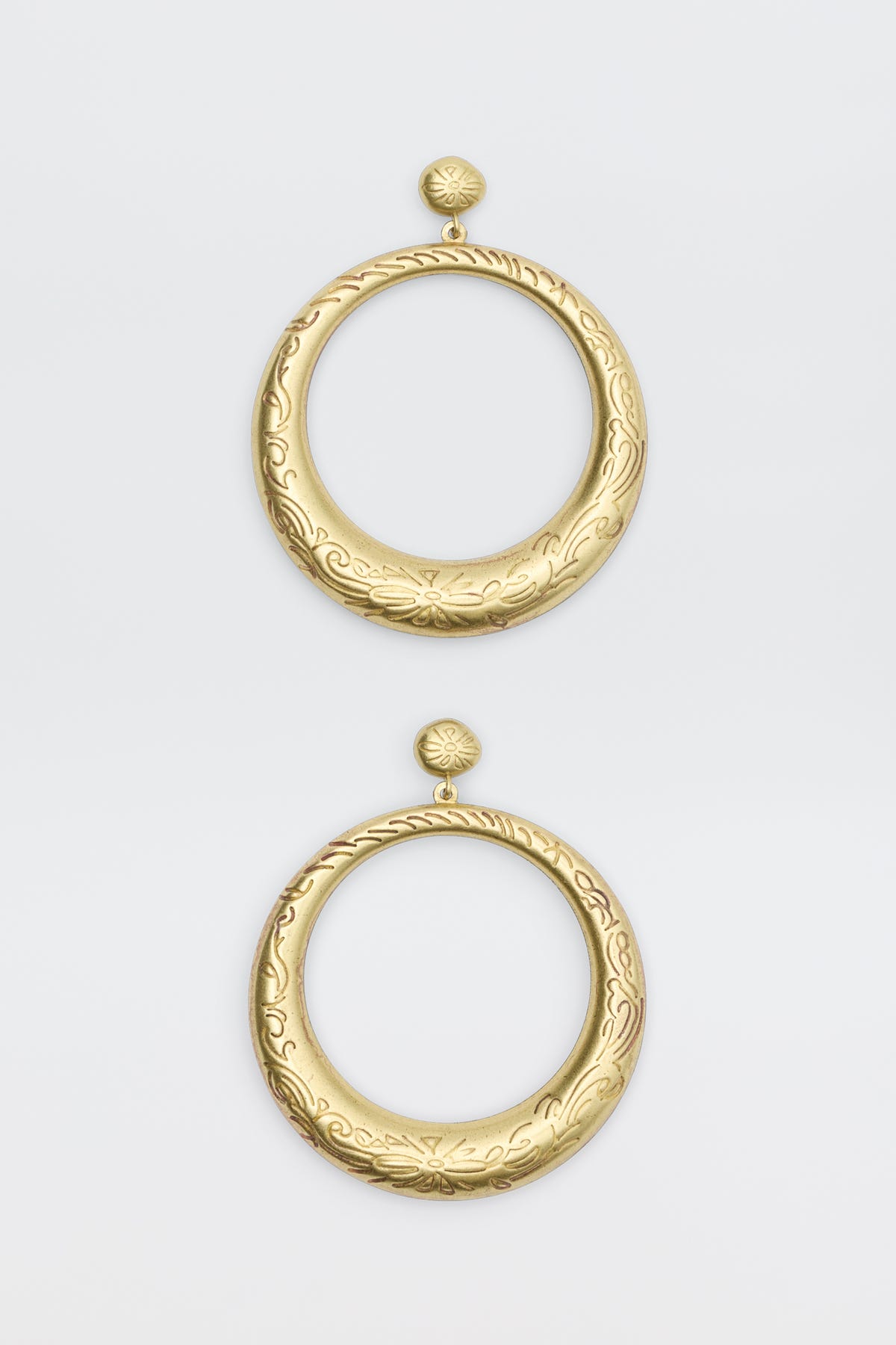 The Sian - Gold earrings are large, circular gold hoops with intricate engraved floral and swirl patterns. Each earring features a round stud top connected to a wide open hoop, displayed on a plain white background.