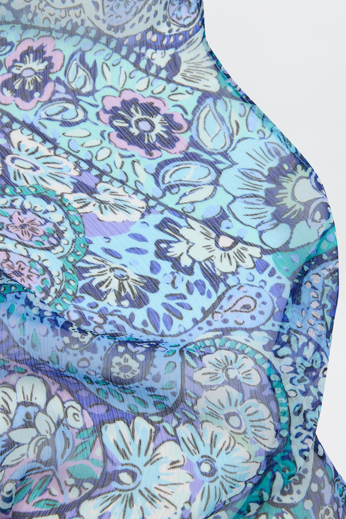 A close-up of Julien - Paisley Floral Blue, a semi-transparent sheer fabric with blue and purple floral and paisley patterns, draped in soft curves against a light background.