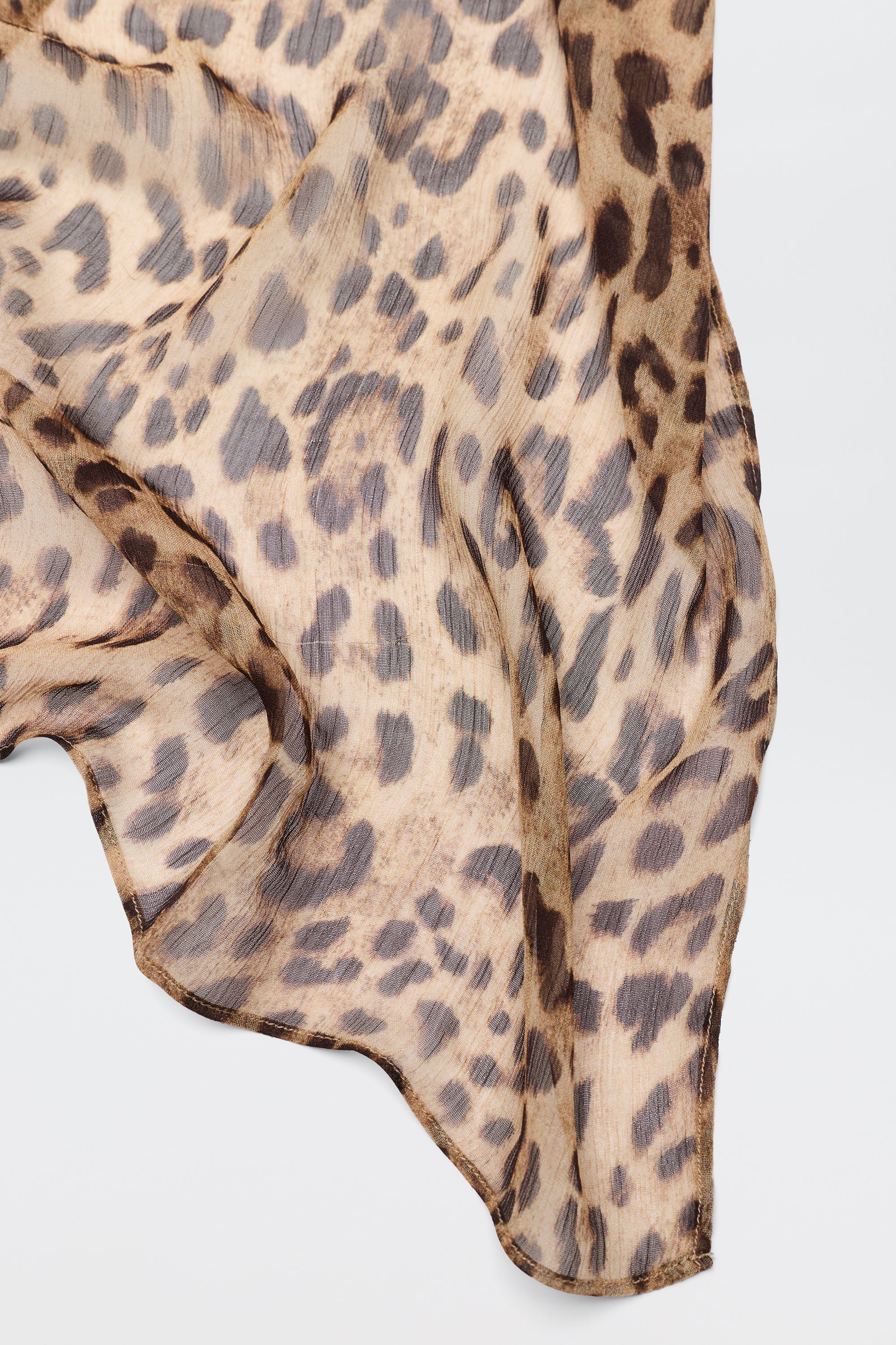 A close-up of the Julien - Mila Leopard Brown scarf shows its lightweight, sheer fabric in neutral brown and black leopard print, elegantly draped against a white background—perfect for a chic accessory.