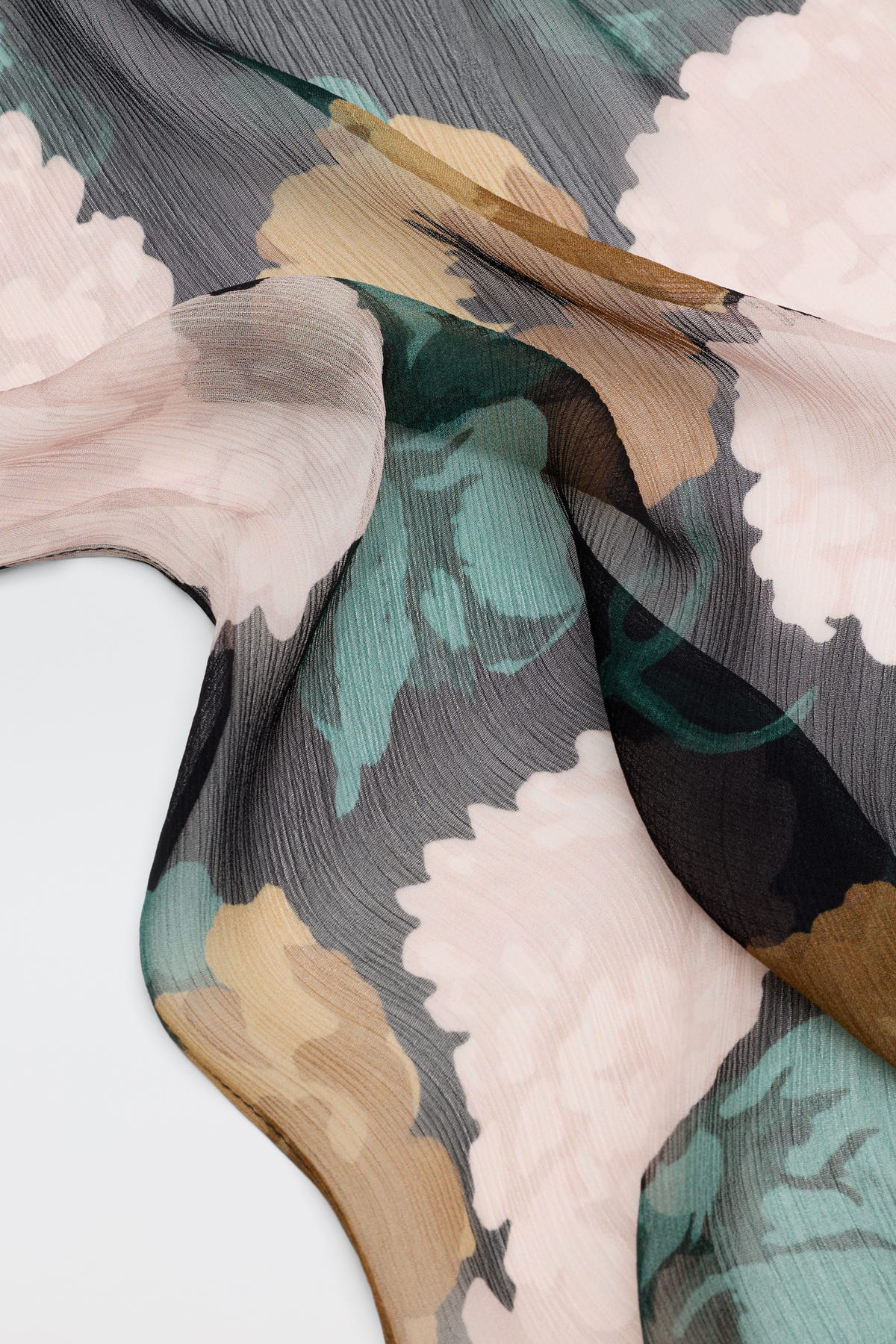 A close-up of Julien - Hydrangea Floral Charcoal sheer fabric, featuring a large hydrangea floral pattern in soft pink, green, beige, and charcoal tones, draped and flowing over a white surface.