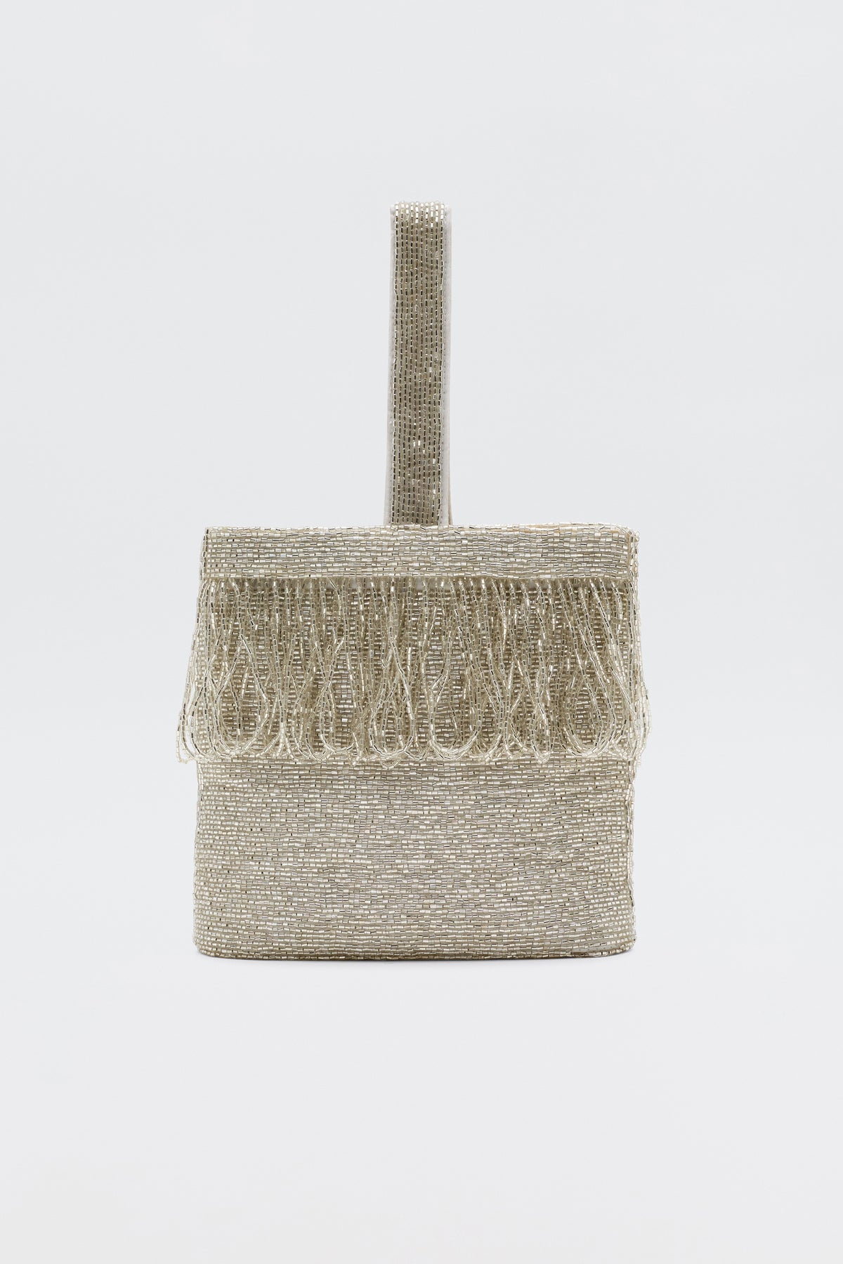 The Zenni - Beaded Silver is a rectangular occasion bag with a rounded top handle and fringe accents, all in metallic silver. It features a silk lining and beaded detailing, displayed against a plain white background.