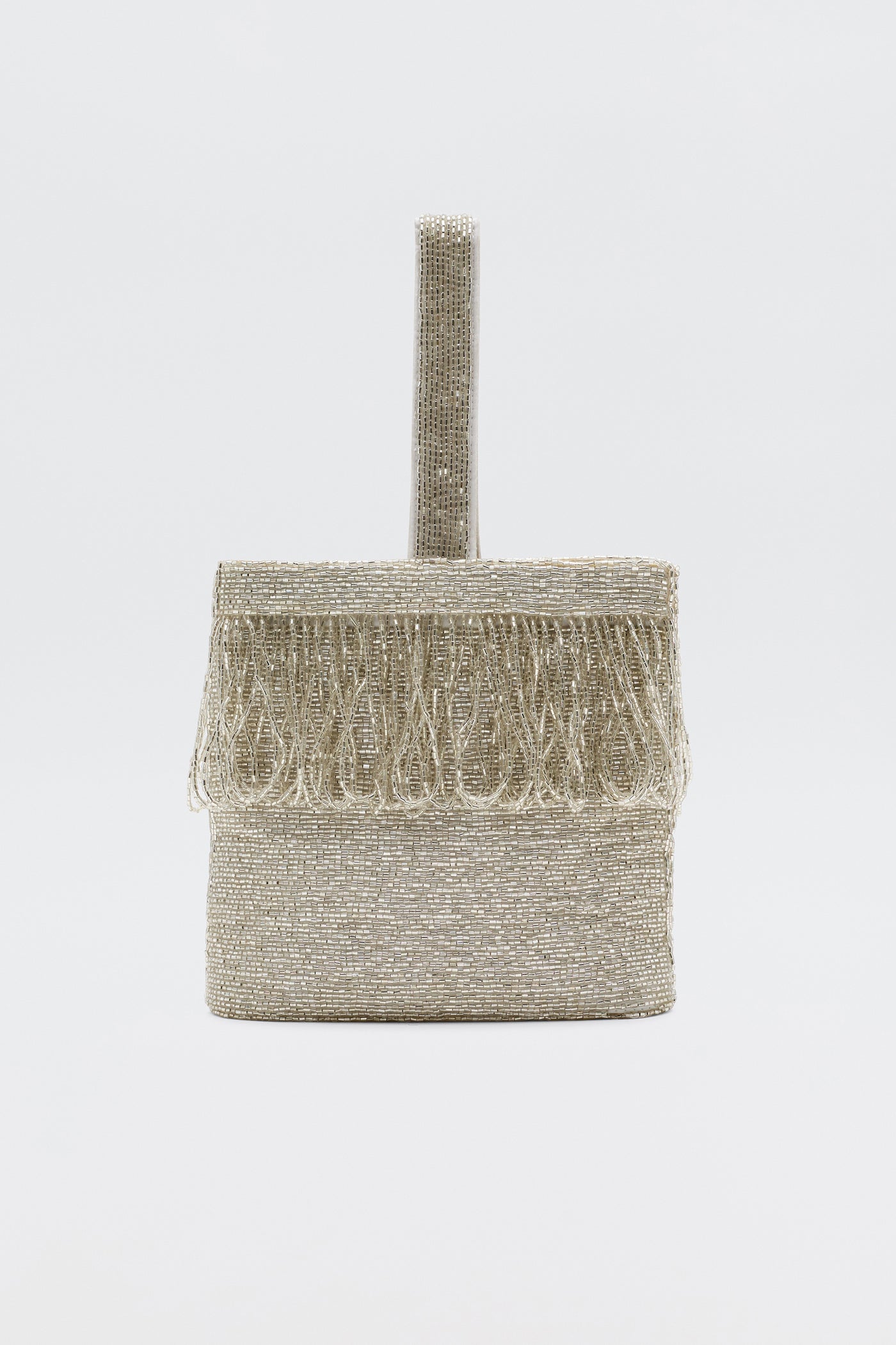 The Zenni - Beaded Silver is a rectangular occasion bag with a rounded top handle and fringe accents, all in metallic silver. It features a silk lining and beaded detailing, displayed against a plain white background.