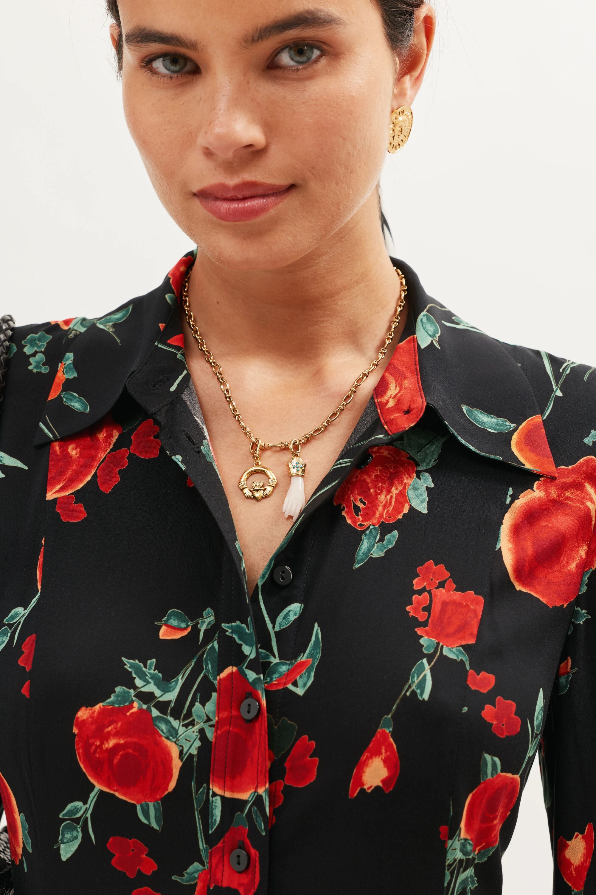 A woman wears the Adara - Gold vintage-inspired jewellery set, including gold earrings and layered gold necklaces with turquoise stones, paired with a black shirt featuring a red floral pattern. She looks slightly to the side with a subtle smile.