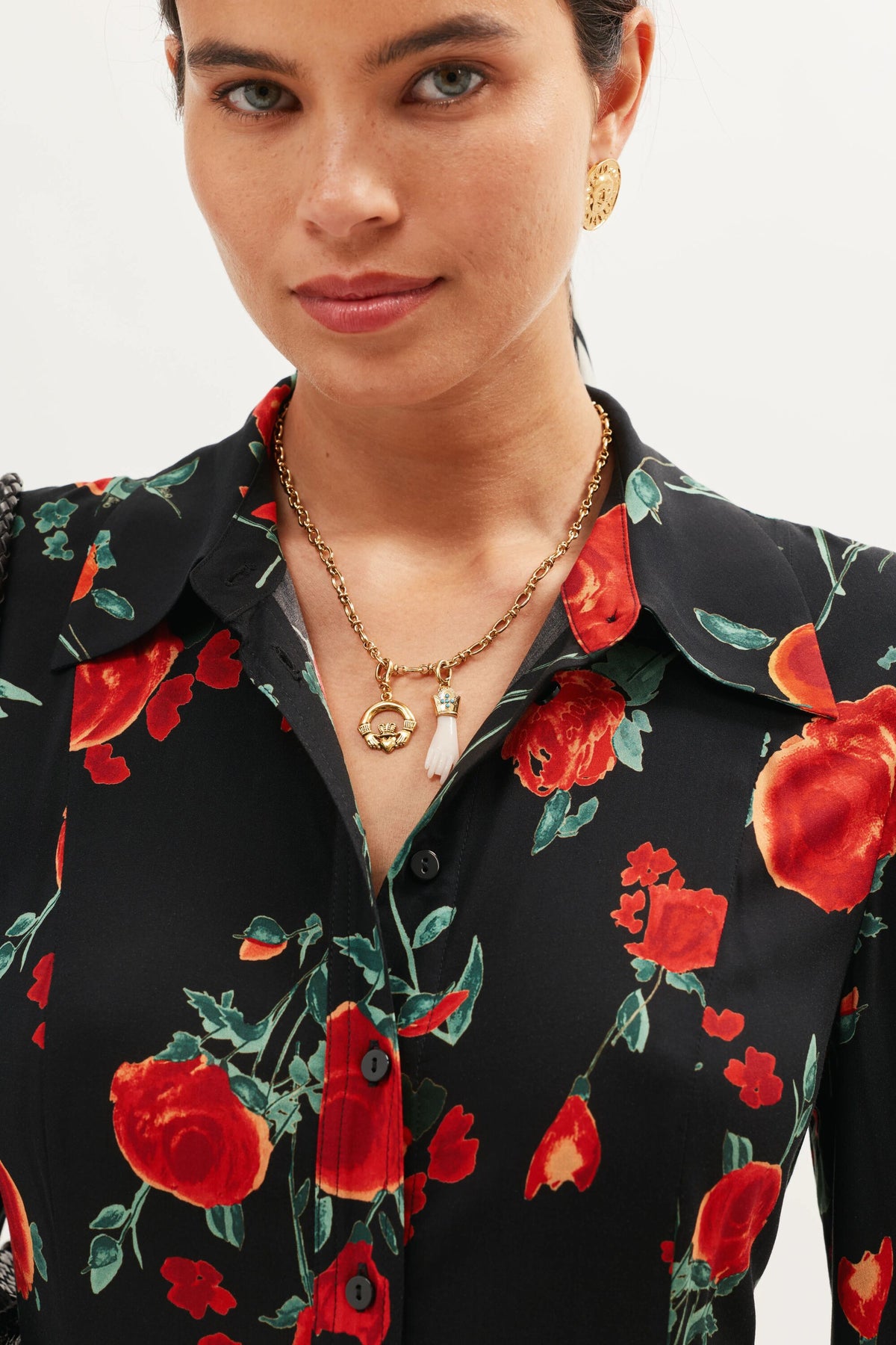 A woman wears the Adara - Gold vintage-inspired jewellery set, including gold earrings and layered gold necklaces with turquoise stones, paired with a black shirt featuring a red floral pattern. She looks slightly to the side with a subtle smile.