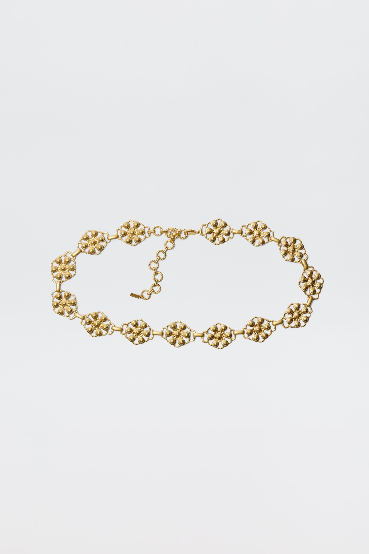 The Tiana - Gold necklace showcases vintage-gold plating with linked, textured floral motifs and an adjustable chain clasp, styled like a daisy-chain belt and displayed against a plain white background.