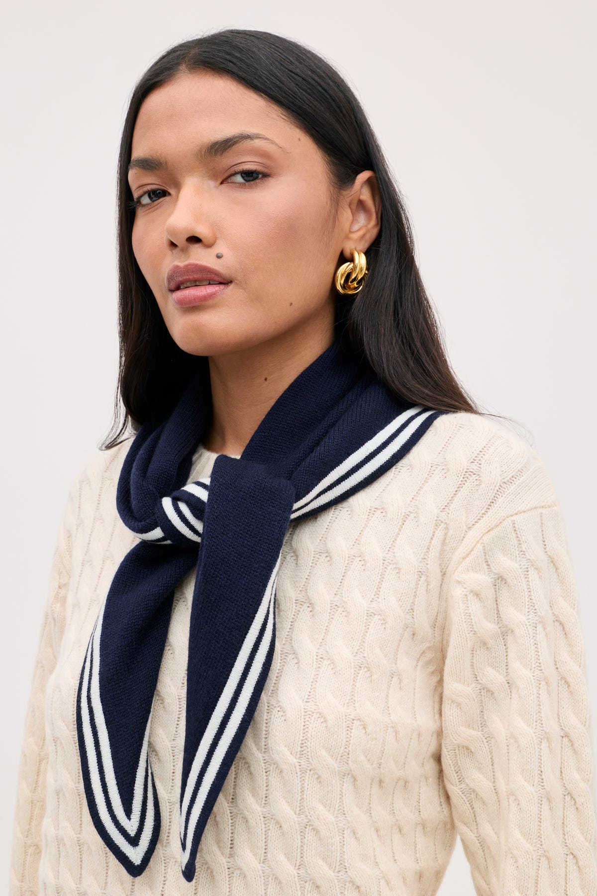 A person wears a cream cable-knit sweater with a Lianora - Sailor Stripe Navy scarf tied around their shoulders.