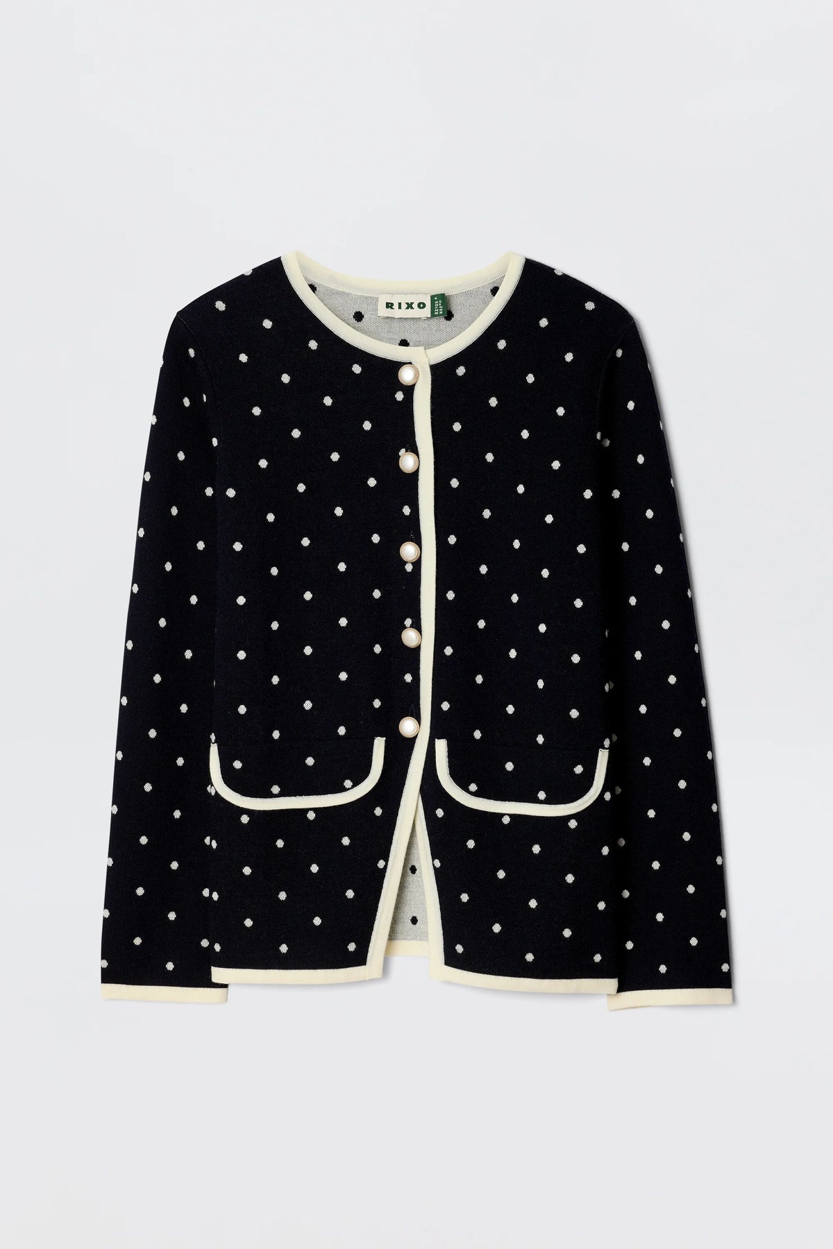The Mirja - City Spot Jacquard Navy cardigan showcases a playful polka dot pattern on soft navy merino wool, cream trim, front pockets, and pearl-like buttons, blending classic elegance with cozy comfort.