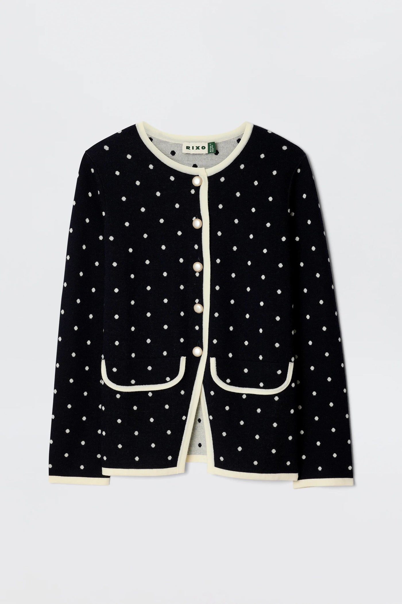 The Mirja - City Spot Jacquard Navy cardigan showcases a playful polka dot pattern on soft navy merino wool, cream trim, front pockets, and pearl-like buttons, blending classic elegance with cozy comfort.