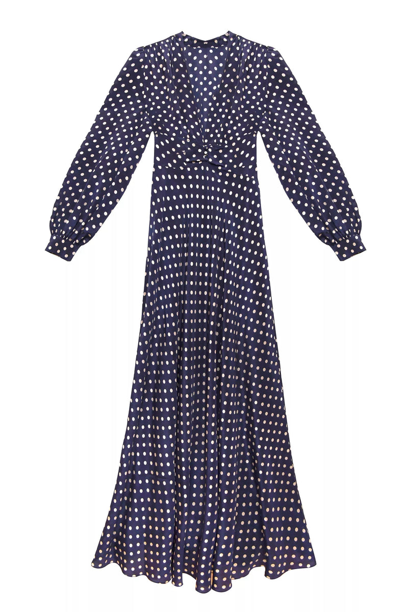 The Emory - Runway Spot Navy is a long-sleeved, floor-length dress with a fitted waist, featuring classic white polka dots on a navy background.