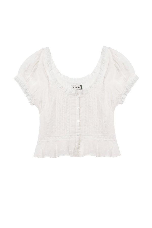 The Sandi - Ivory is a white, short-sleeve cropped blouse with a scoop neckline, button-down front, ruffled hem, lace inserts, and delicate textured detailing for effortless everyday style.