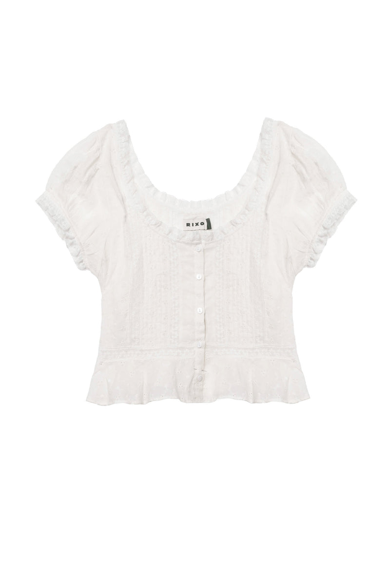The Sandi - Ivory is a white, short-sleeve cropped blouse with a scoop neckline, button-down front, ruffled hem, lace inserts, and delicate textured detailing for effortless everyday style.