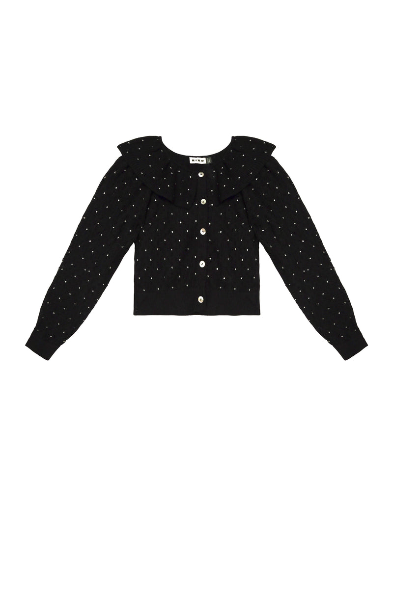 The Jelena - Crystal Black is a black long-sleeve pointelle-knit cardigan with white polka dots, front white buttons, and a large ruffled collar. Its classic and feminine design makes it an elegant choice for parties.