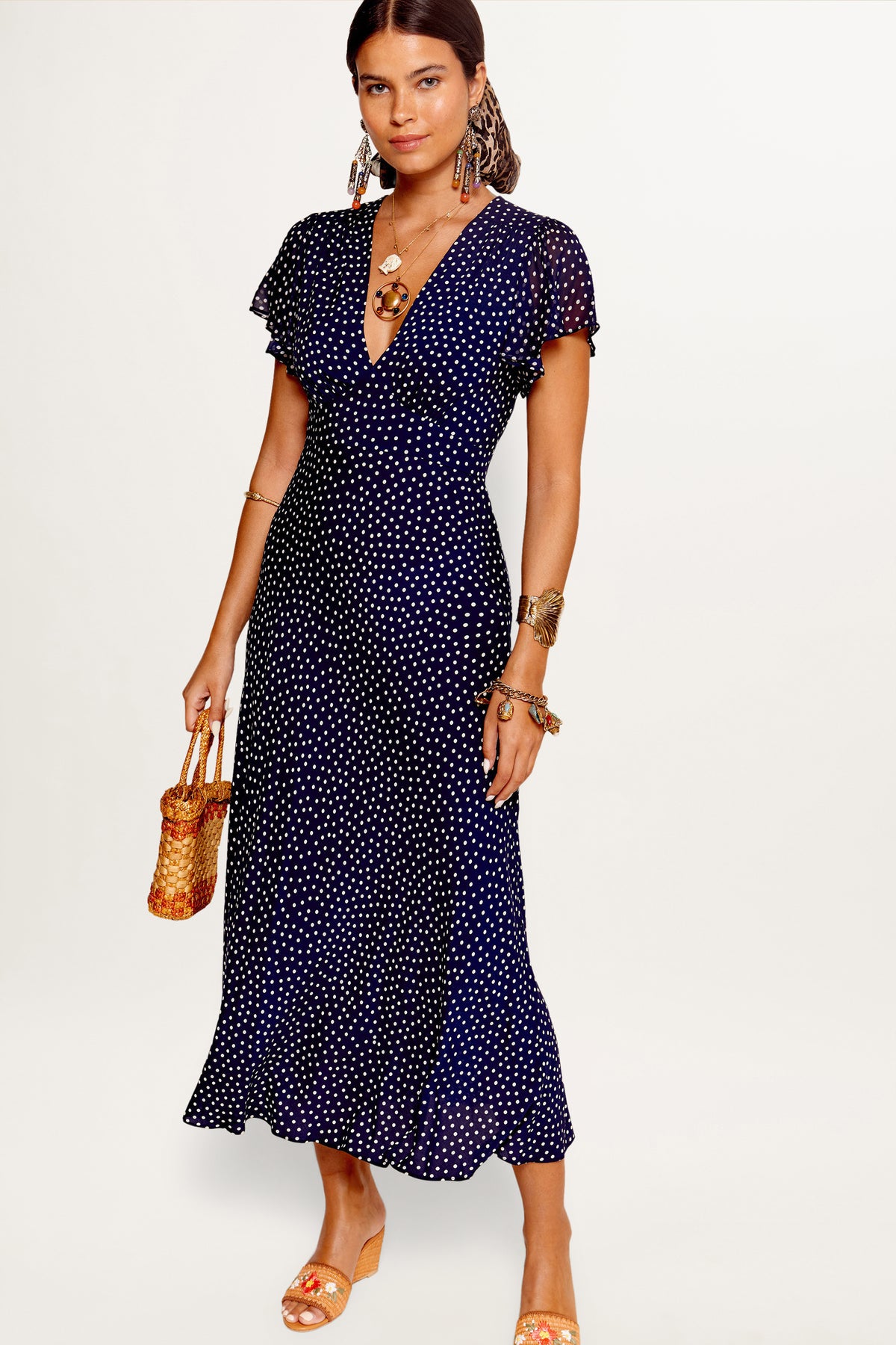 A model wearing a navy dress with a mini polka dot pattern, featuring a V-neck, short sleeves, and a midi length.