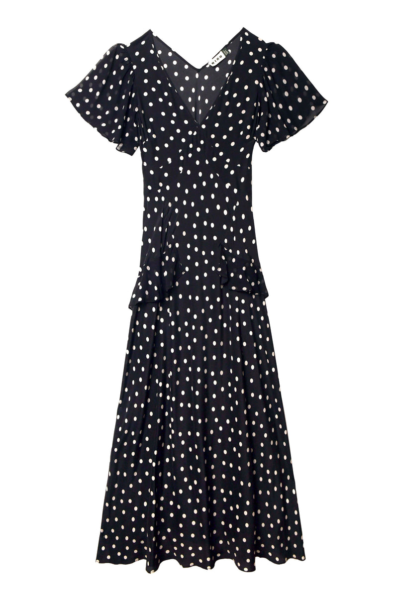 The Evie - Bohemia Spot Deep Navy is a black, short-sleeved, V-neck dress with white polka dots, a fitted waist, ruffled sleeves, and a flared skirt.