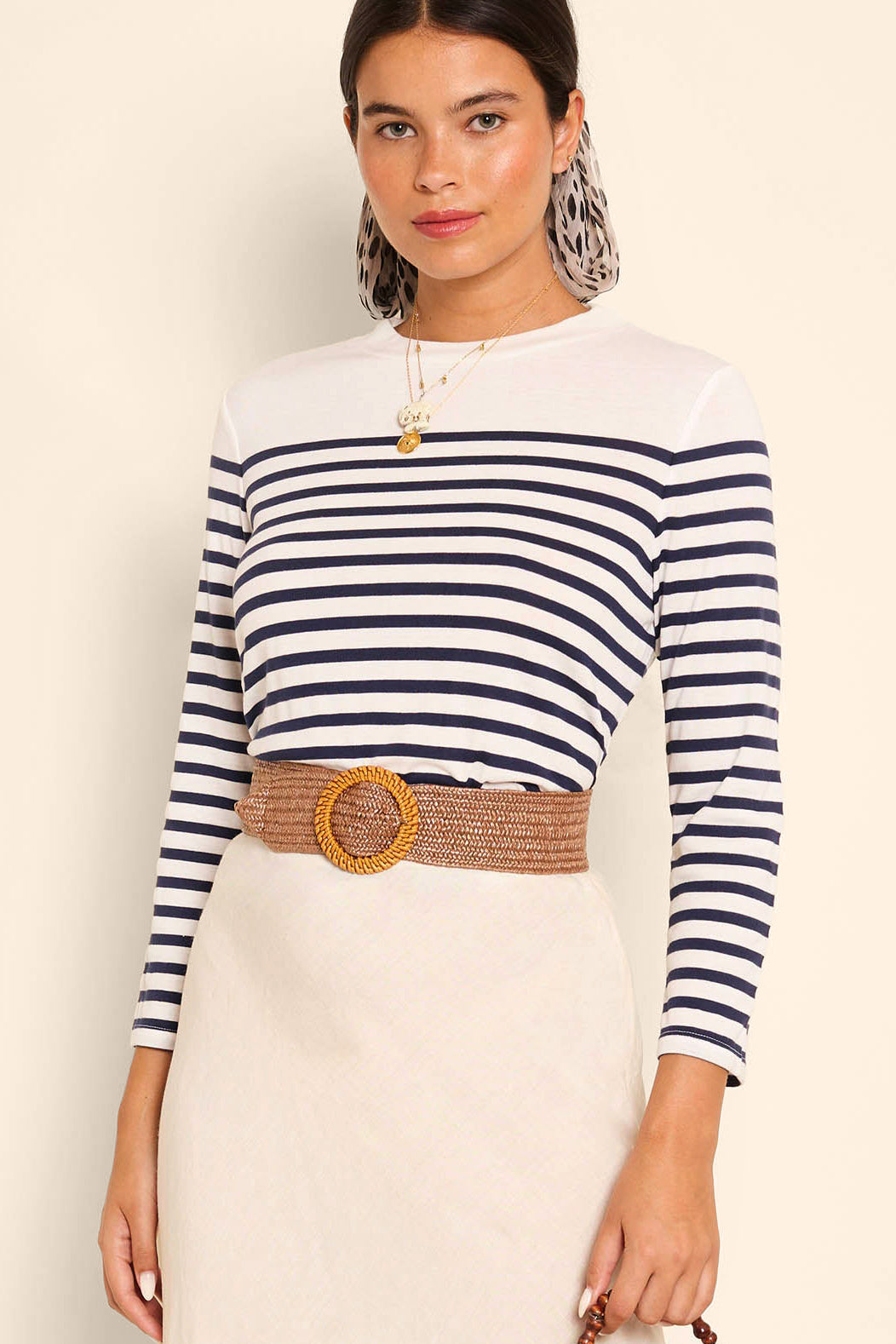 A woman wears the Francesco - Nautical Stripe Cream top with a beige skirt, wide woven belt, layered necklaces, and a printed scarf tied in her hair.