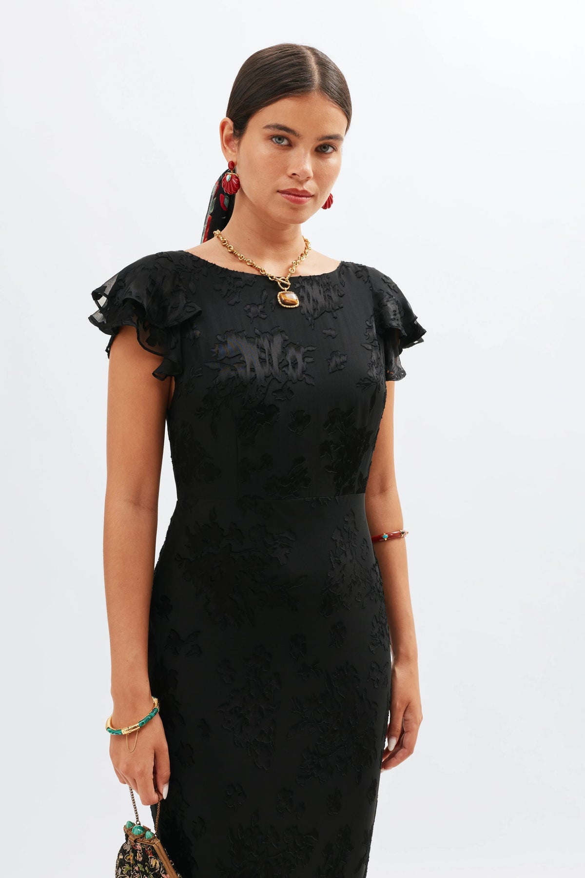 A woman models the fitted Ordinia - Bouquet Devoré Black gown with ruffled sleeves, her hair pulled back, red earrings, and a small handbag—radiating 1930s-inspired elegance ideal for black-tie weddings.