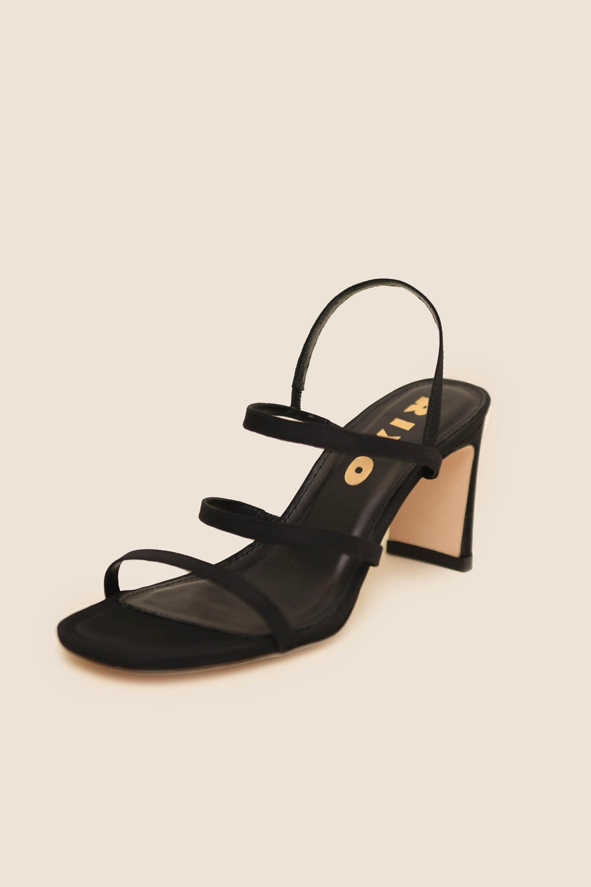 The Ciervo - Black is a vintage-inspired high-heeled sandal featuring black leather, three thin straps across the foot, and an ankle strap, shown on a plain beige background.