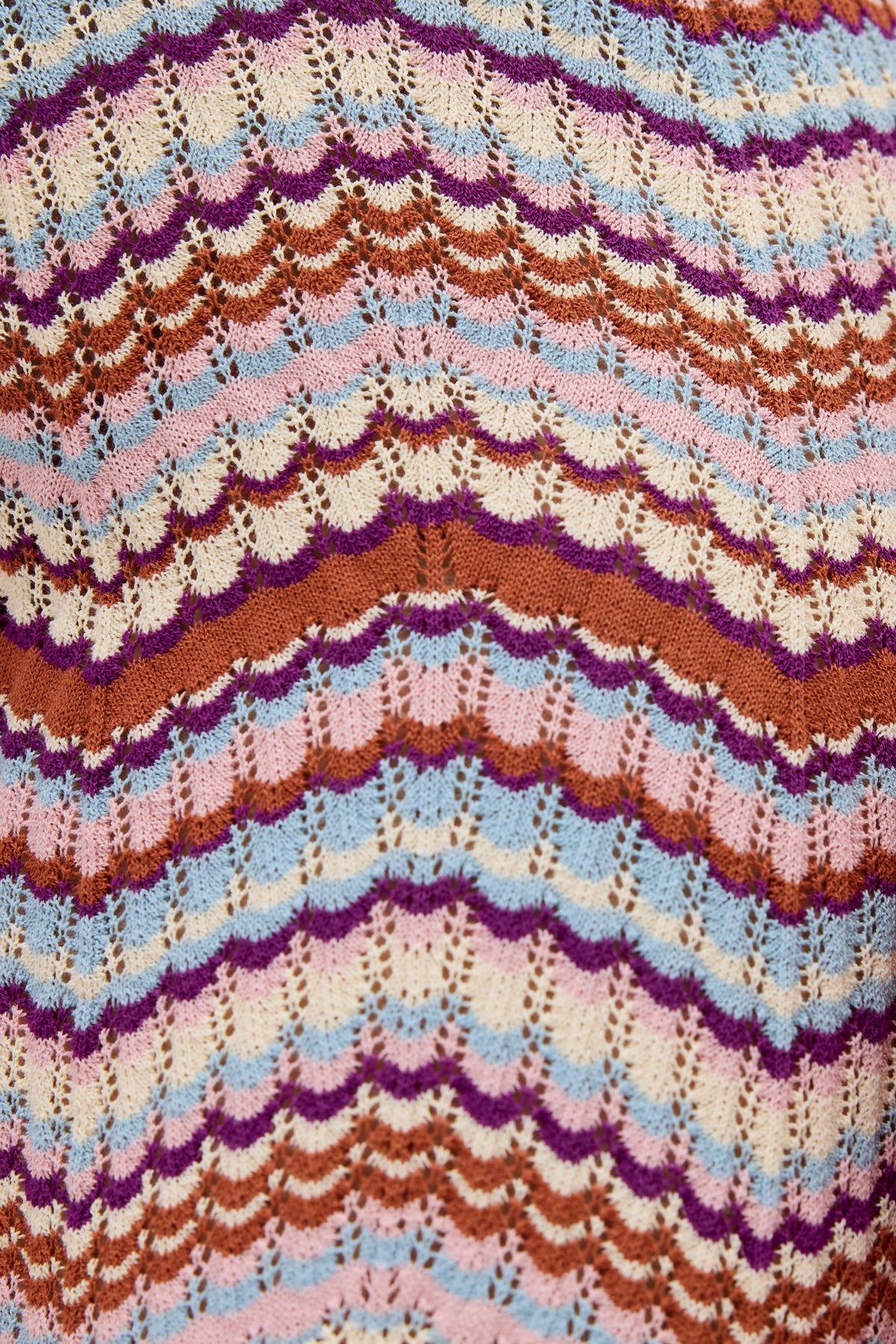 Close-up of Boni - Maria Chevron Multi, a knitted fabric featuring wavy, scalloped stripes in brown, pink, yellow, lavender, and blue. Crafted from breathable cotton, this fabric boasts an intricate repeating lace design that creates a colorful and textured pattern—perfect for versatile wardrobe pieces like knitted trousers.