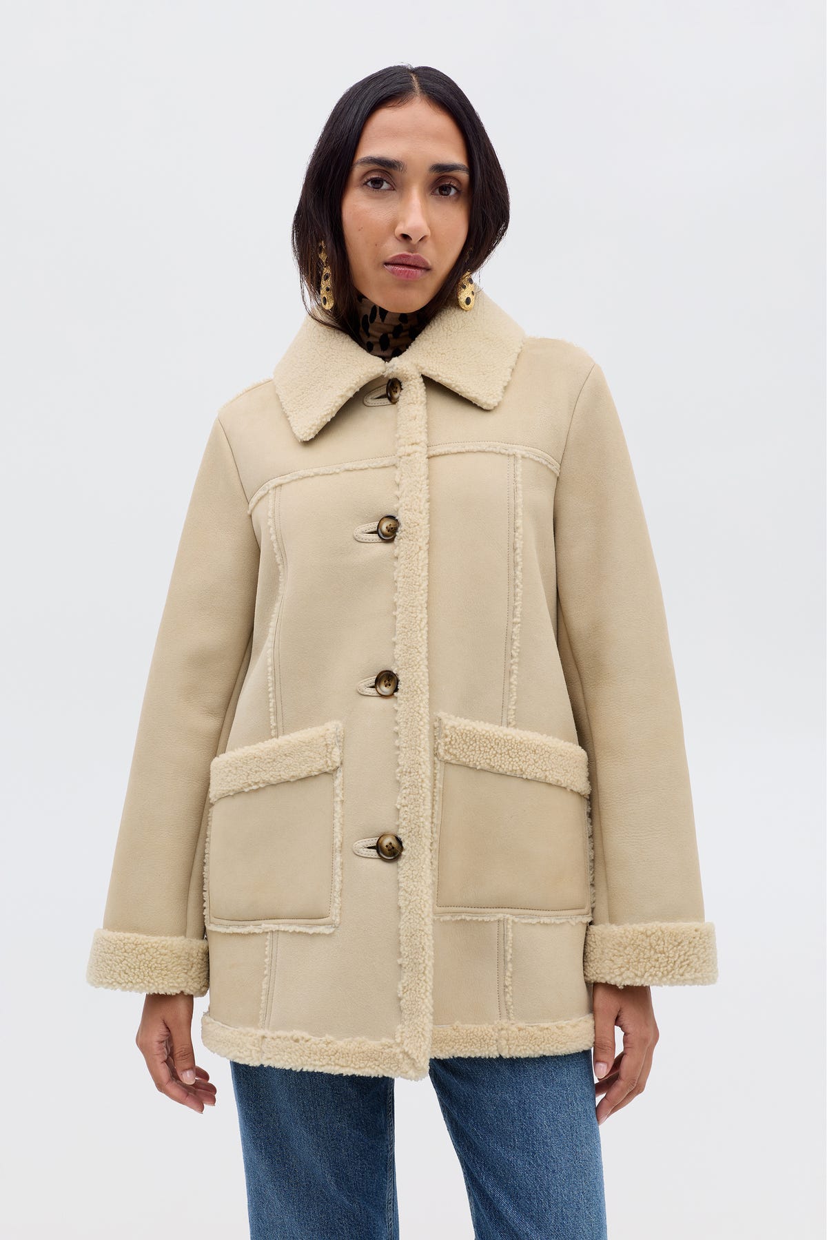 A woman wears the Ellis - Cream faux-shearling coat with front pockets and button closures, styled with blue jeans against a light background—ideal autumn outerwear.