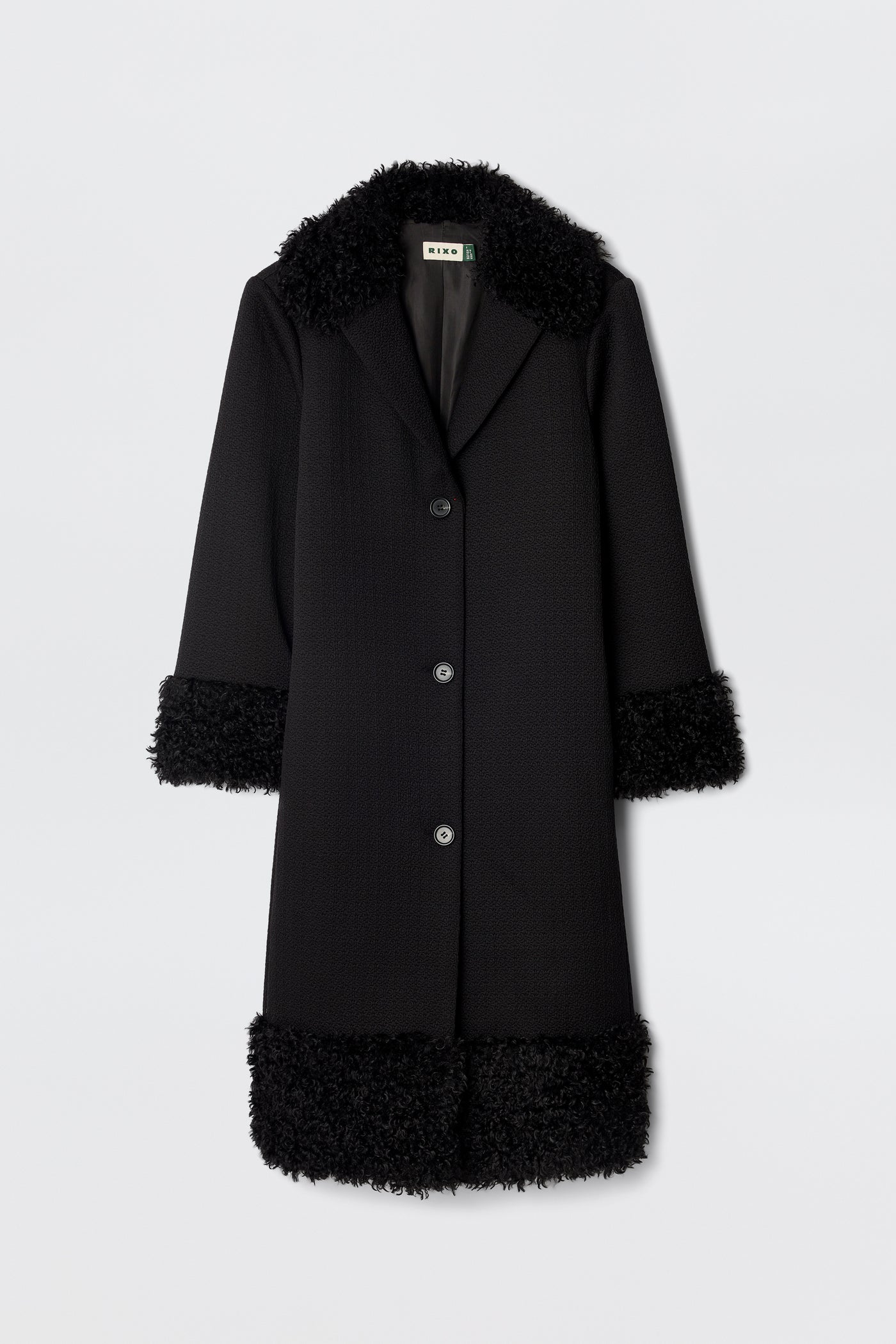 The Diara - Black is a long, black 70s-style coat with three buttons and fluffy faux-fur shearling trim on the collar, cuffs, and hem, shown against a plain white background.