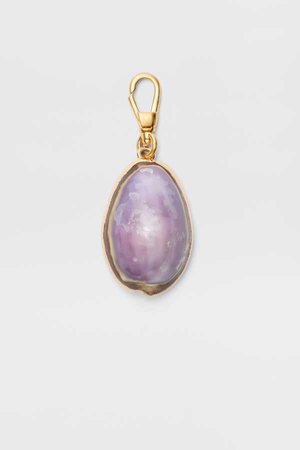 Cowrie - Lavender: An elegant bohemian pendant with a gold clasp and frame, showcasing a polished oval purple stone with white and light pink marbling, set against a plain light background.