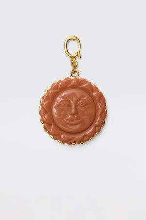 The Lillias - Orange is a round vintage charm pendant featuring a carved orange sun with a smiling face, surrounded by a gold scalloped border and attached to a gold clasp, displayed on a plain white background.