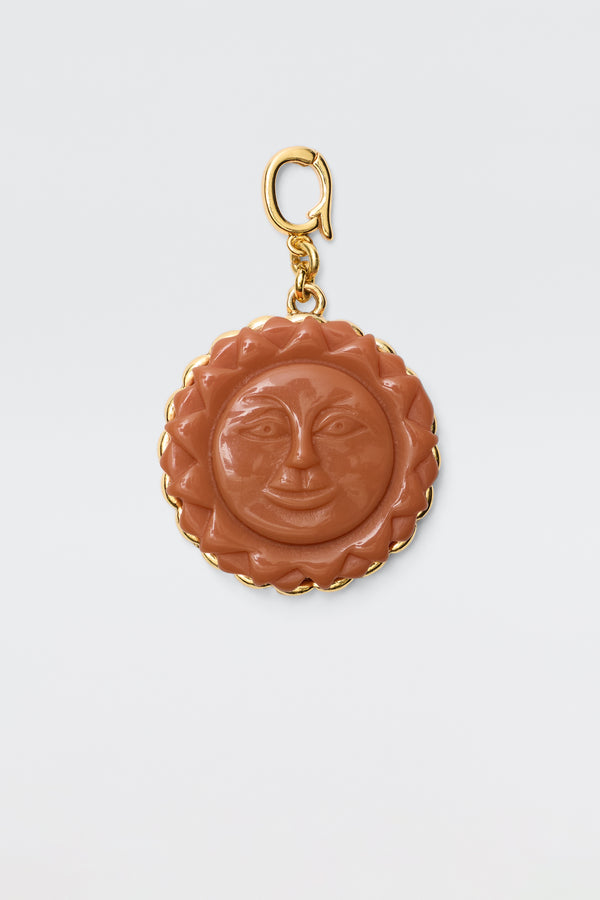 The Lillias - Orange is a round vintage charm pendant featuring a carved orange sun with a smiling face, surrounded by a gold scalloped border and attached to a gold clasp, displayed on a plain white background.