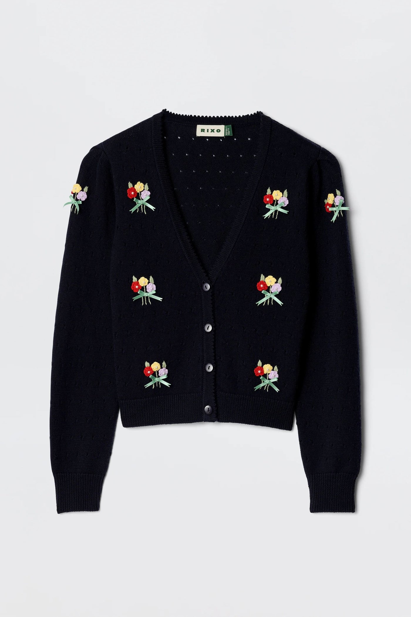 The Merinda - Floret Embroidery Deep Navy is a V-neck black cardigan with button closure, featuring colorful bouquet embroidery on the front and sleeves, a textured knit pattern, and ribbed cuffs and hem for a classic finish.