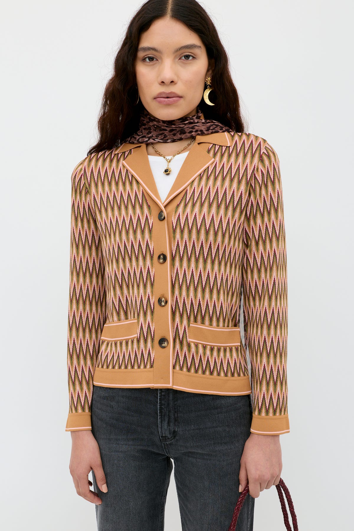 A woman wears the Quinley - Maeve Jacquard Multi cardigan over a white top with dark jeans, gold earrings, layered necklaces, and a brown scarf, standing against a plain white background.