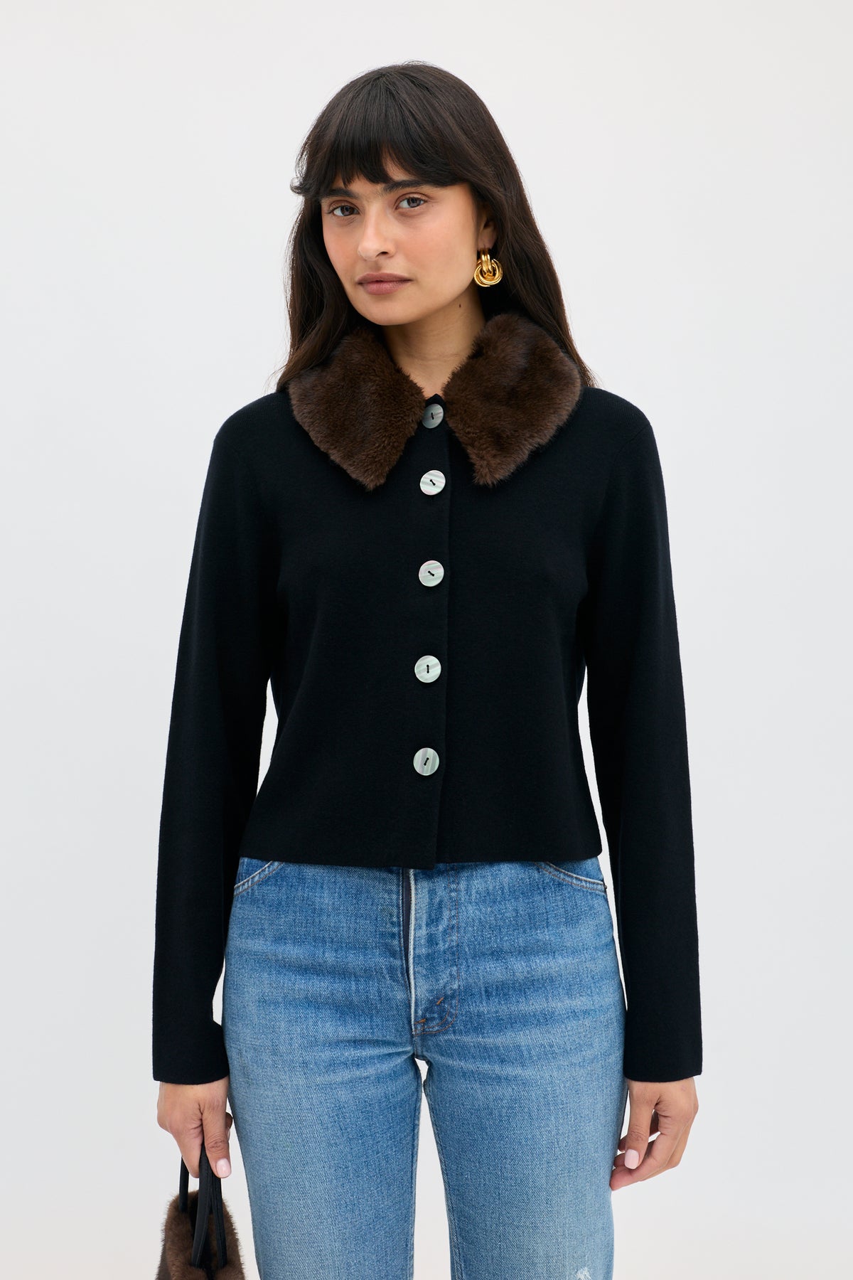 A person wears a Jasmin - Black button-down cardigan with a dark brown faux-fur collar over blue jeans.