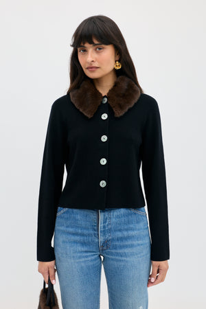 A person wears a Jasmin - Black button-down cardigan with a dark brown faux-fur collar over blue jeans.