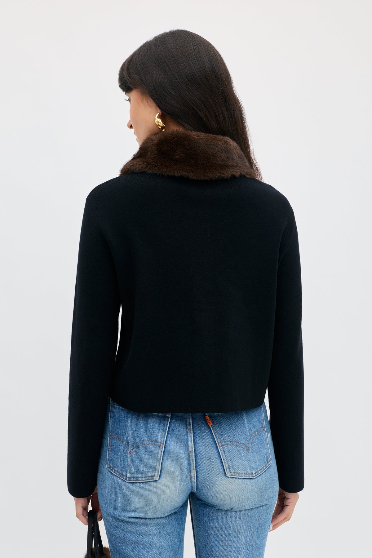 Back view of the Jasmin - Black long-sleeved top with a dark brown faux fur collar, worn with blue jeans.