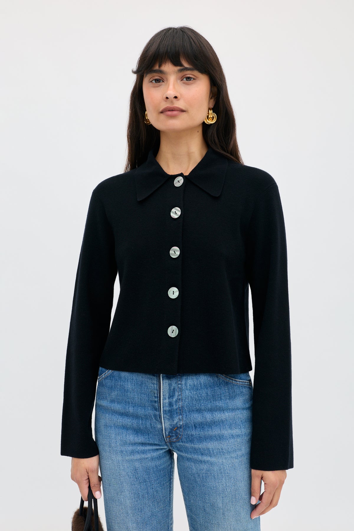 A woman wearing a Jasmin - Black long-sleeved button-up cardigan with a collar and blue jeans.