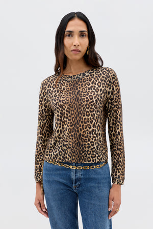 A woman with long brown hair wears the Phaedra - Lyra Leopard Black crop top, blue jeans, gold earrings, and a gold chain belt, standing against a plain light background.
