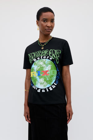 A person with short hair wears the Charity - Rixo x War Child x Before Midnight Black T-shirt with a green and blue earth motif and VOICES AS ONE BEFORE MIDNIGHT text, styled with a necklace, earrings, and black skirt—ideal for the festival.